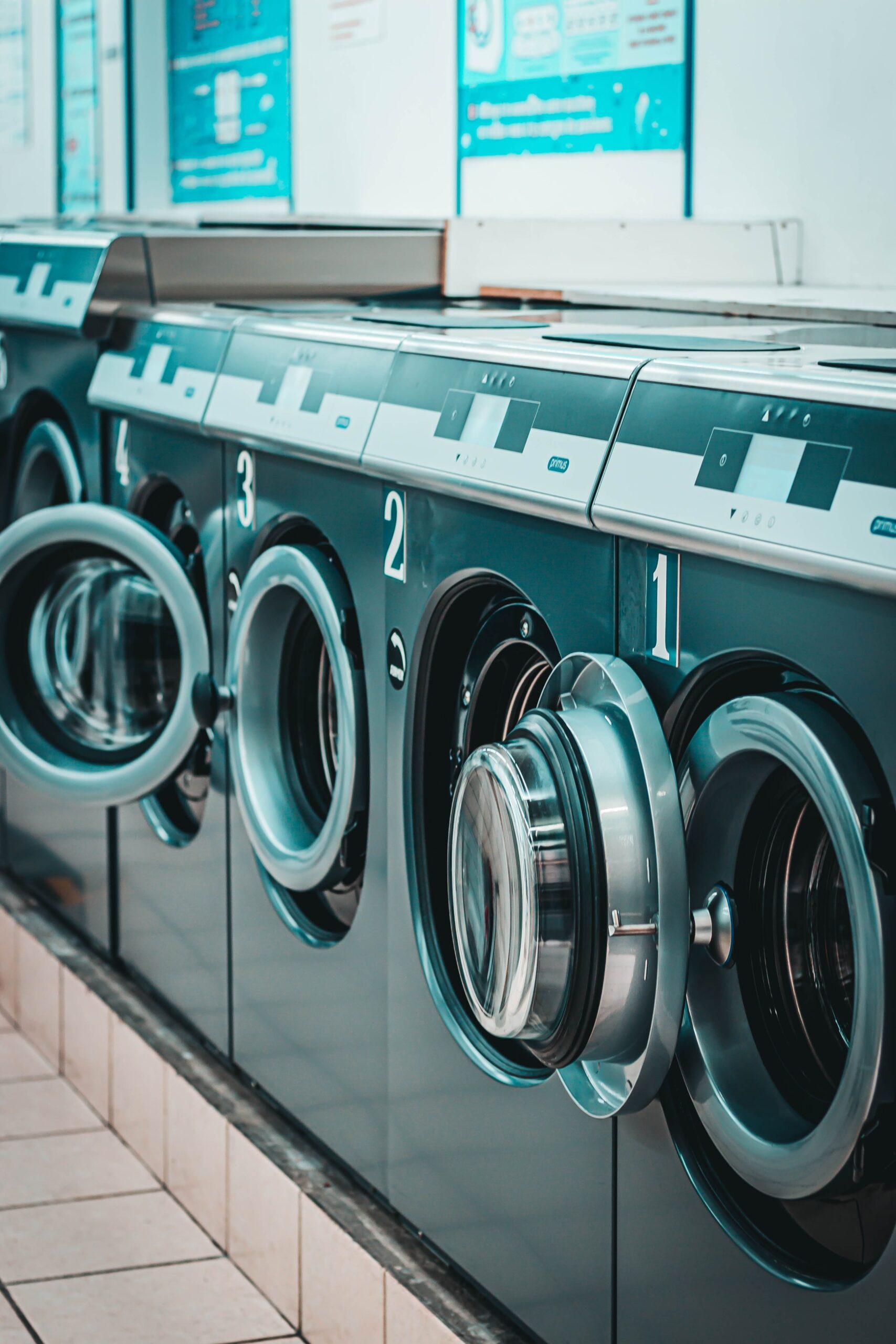 Row of contemporary numbered washing machines placed on tiled floor in light laundry